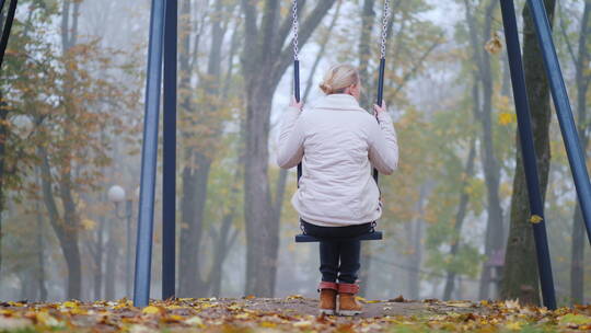 一个女人坐在公园秋千上的后视图