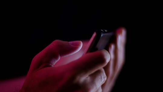 当视频在黑暗的房间侧面特写中播放时，拇指在智能手机上视频素材模板下载