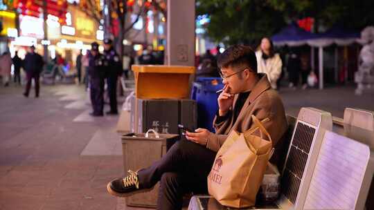 男子夜晚街边独坐抽烟玩手机