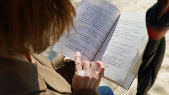 年轻女性坐在海边阅读书籍视频素材模板下载