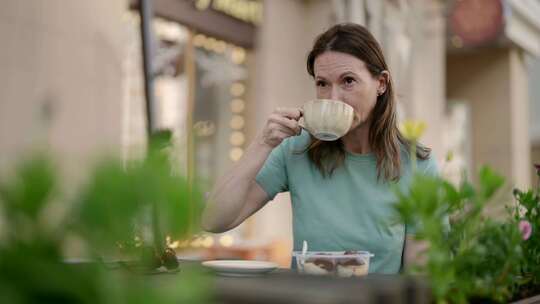 一位中年妇女在户外咖啡馆喝咖啡，吃甜点，