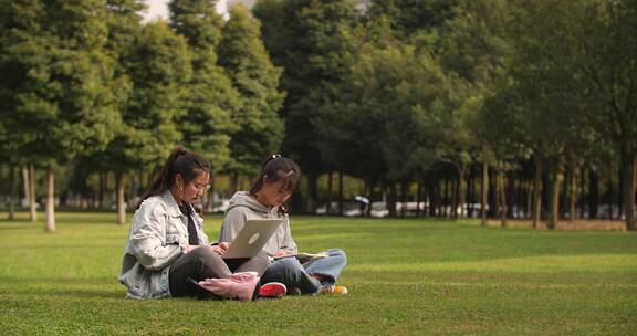 两位女大学生在校园草地上用电脑学习