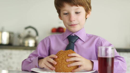 小男孩坐在桌旁大口吃汉堡