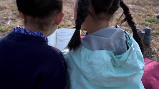 冬季在公园草坪上看书的两个女孩视频素材模板下载