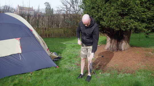 一个男人在野外露营时，在帐篷旁边把帐篷杆