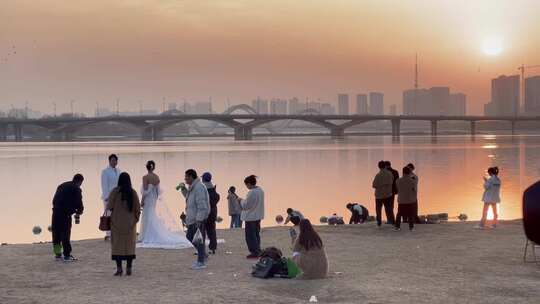 落日余晖河边人工沙滩拍婚纱游玩的人