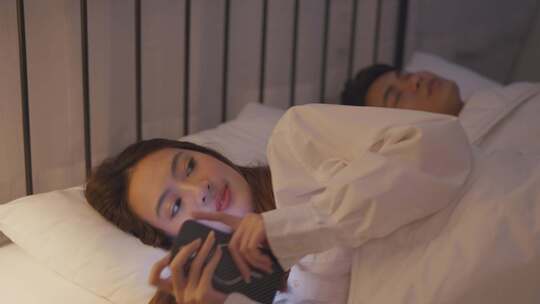 亚洲女人和丈夫躺在床上偷偷和情人聊天。