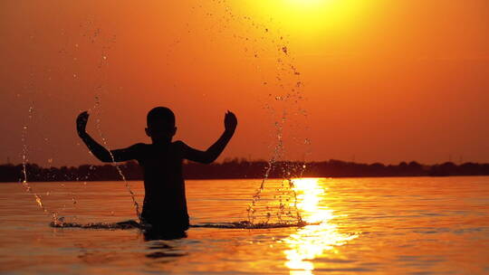 日落时男孩在水中玩乐