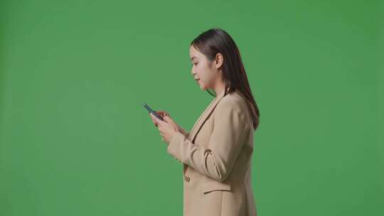 亚洲女商人使用手机和走在绿屏色度键的侧视图