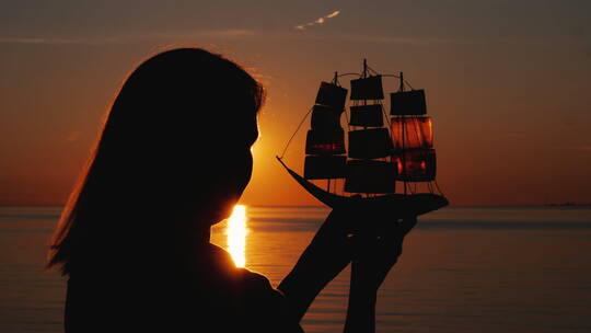 日落时分女人拿着帆船模型在海边