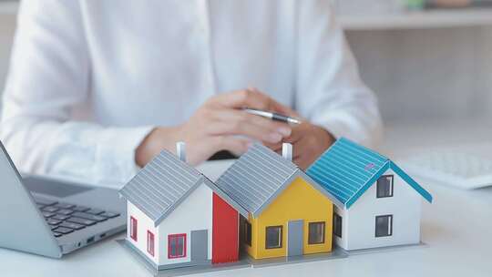 人手持笔在电脑旁查看房屋模型