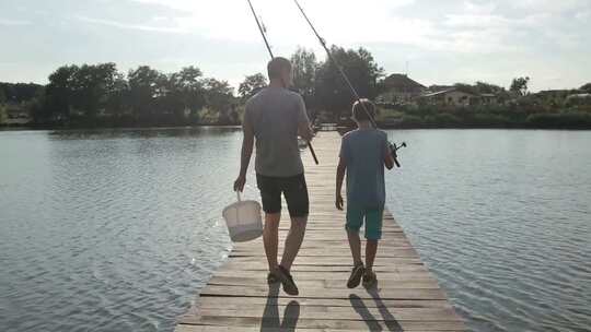 父子拿着鱼竿走在湖边栈道、钓鱼