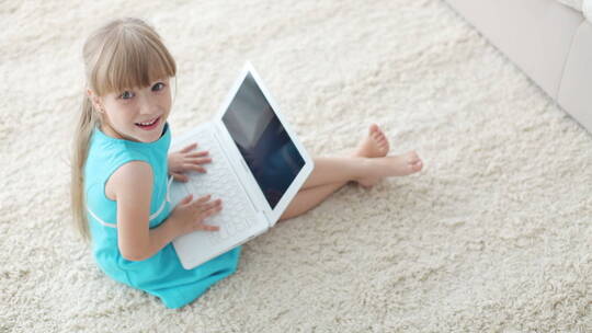 小女孩坐在地毯上玩笔记本电脑