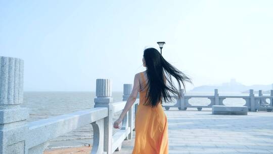 长发女孩在海滨公园吹风行走的背影