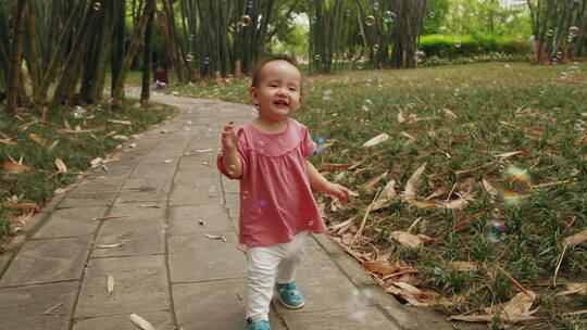 蹒跚学步的可爱小婴儿在公园里玩耍抓泡泡