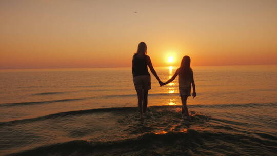 夕阳下母女牵手走在海水里视频素材模板下载