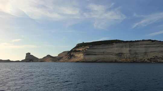 帆船船头朝向科西嘉岛悬崖和法国Capo Pertusato灯塔航行，