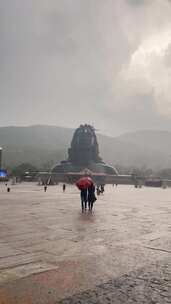 一个人在雨中行走，背景是雕像