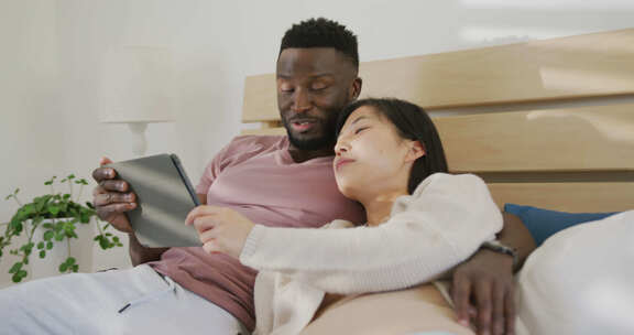 快乐的多样化夫妇使用平板电脑，躺在卧室里