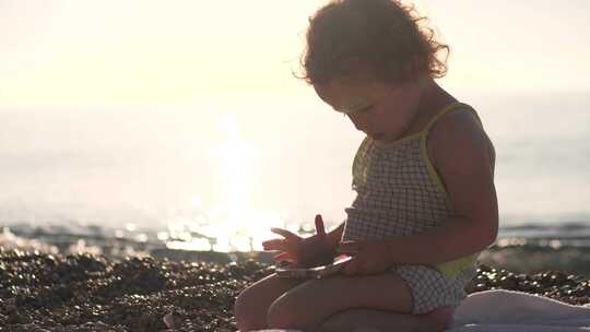 专注的女婴在海滩上使用智能手机