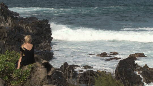 女人坐在海边岩石上吹海风