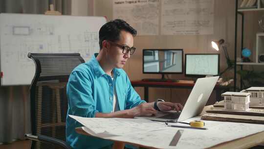 亚洲男工程师在笔记本电脑上打字和看蓝图之前走进办公室