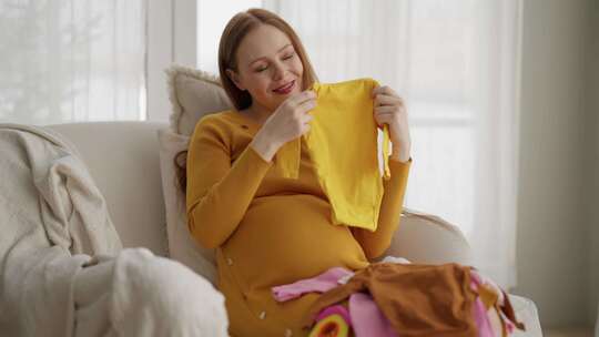 孕妇看着婴儿服装美丽的未来母亲享受分娩看