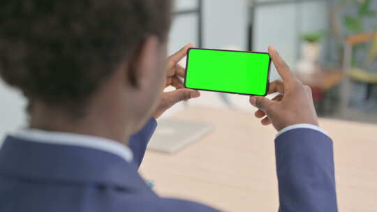 年轻的非洲商人手持带绿屏的水平智能手机