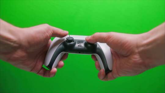 手拿着操纵杆白色游戏手柄的特写镜头在绿色背景下玩现代电子游戏