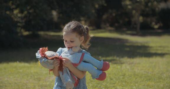 女孩站在草地上拥抱布娃娃
