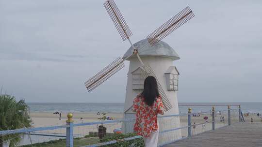 女子站在海边栈道赏风车的场景