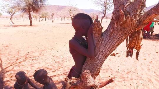 一个年轻的非洲辛巴部落男孩靠在树上