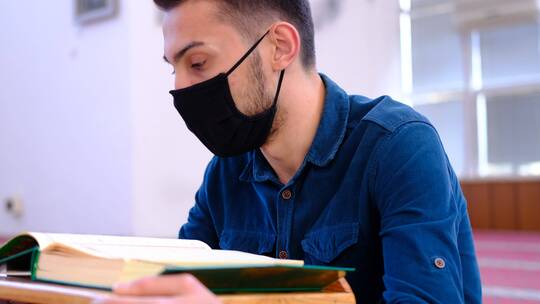 年轻的男子戴着口罩阅读古兰经