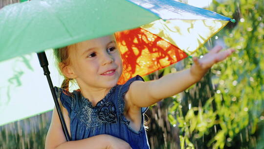 一个无忧无虑的女孩享受雨的肖像它应该在彩虹色的雨伞下