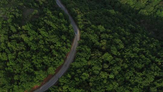 航拍越野车在穿过森林小山的柏油路上行驶