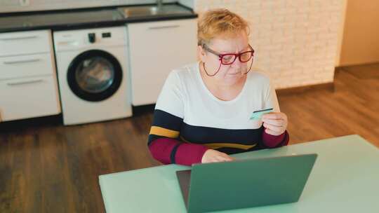 戴眼镜的胖女人使用笔记本电脑和信用卡在家