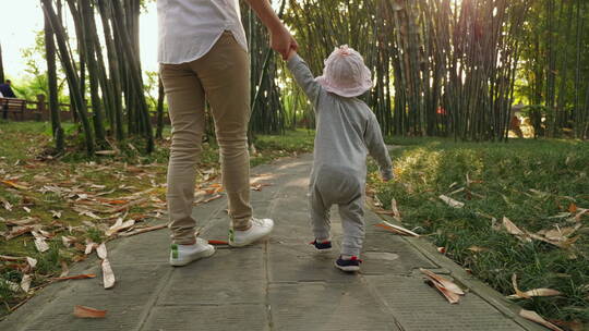 蹒跚学步的小宝宝牵着妈妈的手走在公园小路