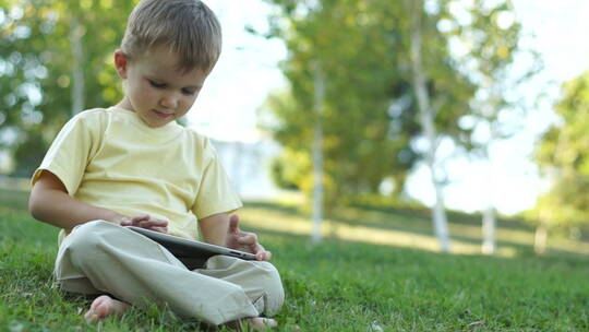 小男孩坐在草坪上玩平板