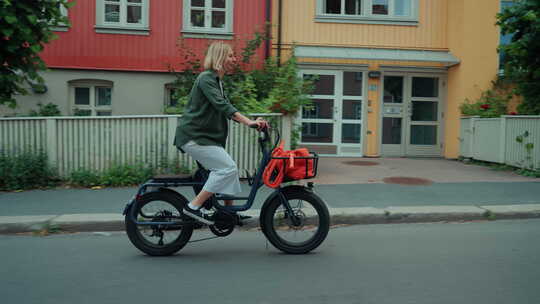 可爱的年轻女子在夏日街上骑城市电动自行车