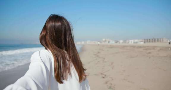 女人牵着男人的手，微笑着走在海滩上，直视