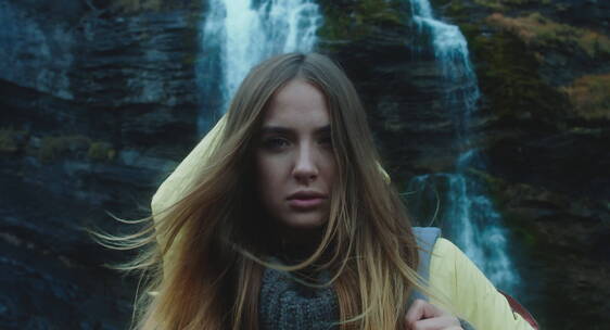 年轻女子站在瀑布前面向镜头