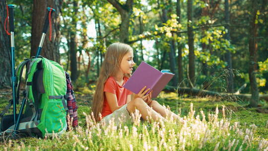 远足女孩坐在草地上微笑着看书