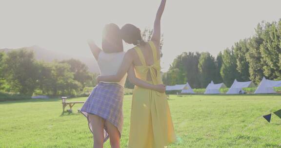 两个美女在露营地的绿色草地上拥抱阳光