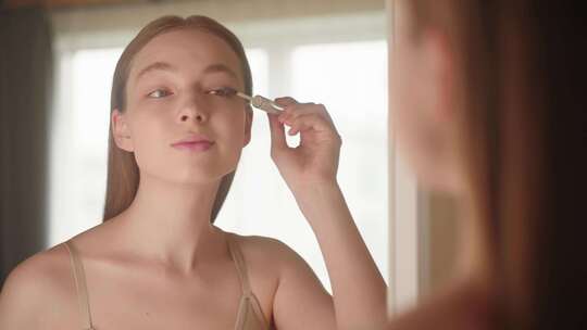 一个女孩照镜子时用刷子在睫毛上涂抹凝胶