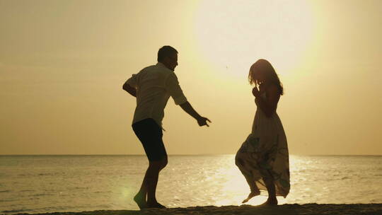 年轻夫妇在大海和落日背景下跳舞的剪影