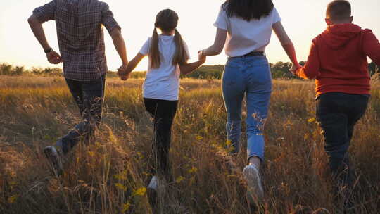日落时分，快乐的父母带着孩子在草地上慢跑，手牵着手