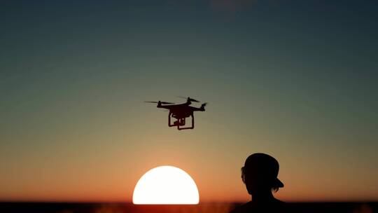 一个男孩在日落时驾驶无人机的剪影