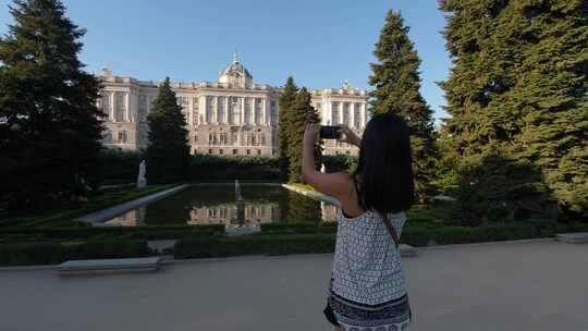一大早，女孩在池塘里用倒影拍摄马德里皇宫的照片