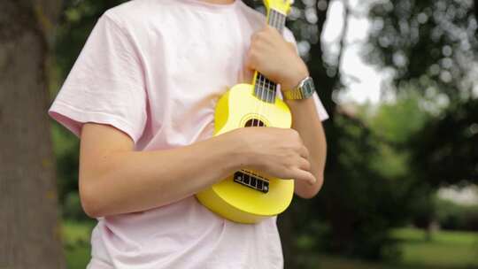 穿着夏装的男孩在公园演奏尤克里里