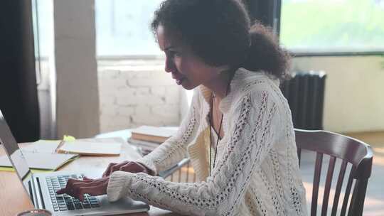 年轻的非裔美国妇女在家庭办公室的桌子上用笔记本电脑工作